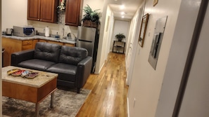 A compact kitchen with a refrigerator, microwave, and coffee maker. A leather sofa and a small table with decorative plates are in the living area.