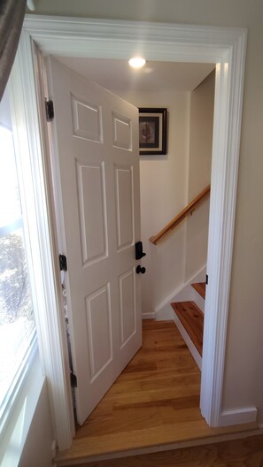 A white door with a black handle, a wooden staircase with a handrail, and a framed picture on the wall.