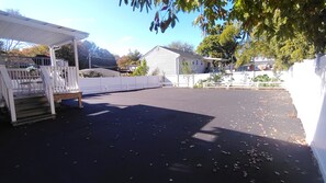 Un espacio exterior cubierto con una terraza de madera, una cerca blanca y un suelo pavimentado cubierto de hojas.