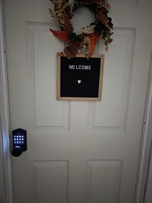 A door with a 'WELCOME' sign, a decorative wreath, and a digital keypad lock.