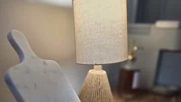 A wooden table with a white cutting board and a lamp with a textured lampshade.