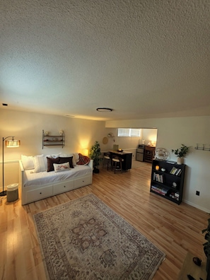 A modern living room with a white sofa, a patterned rug, a desk with chairs, and a bookshelf.