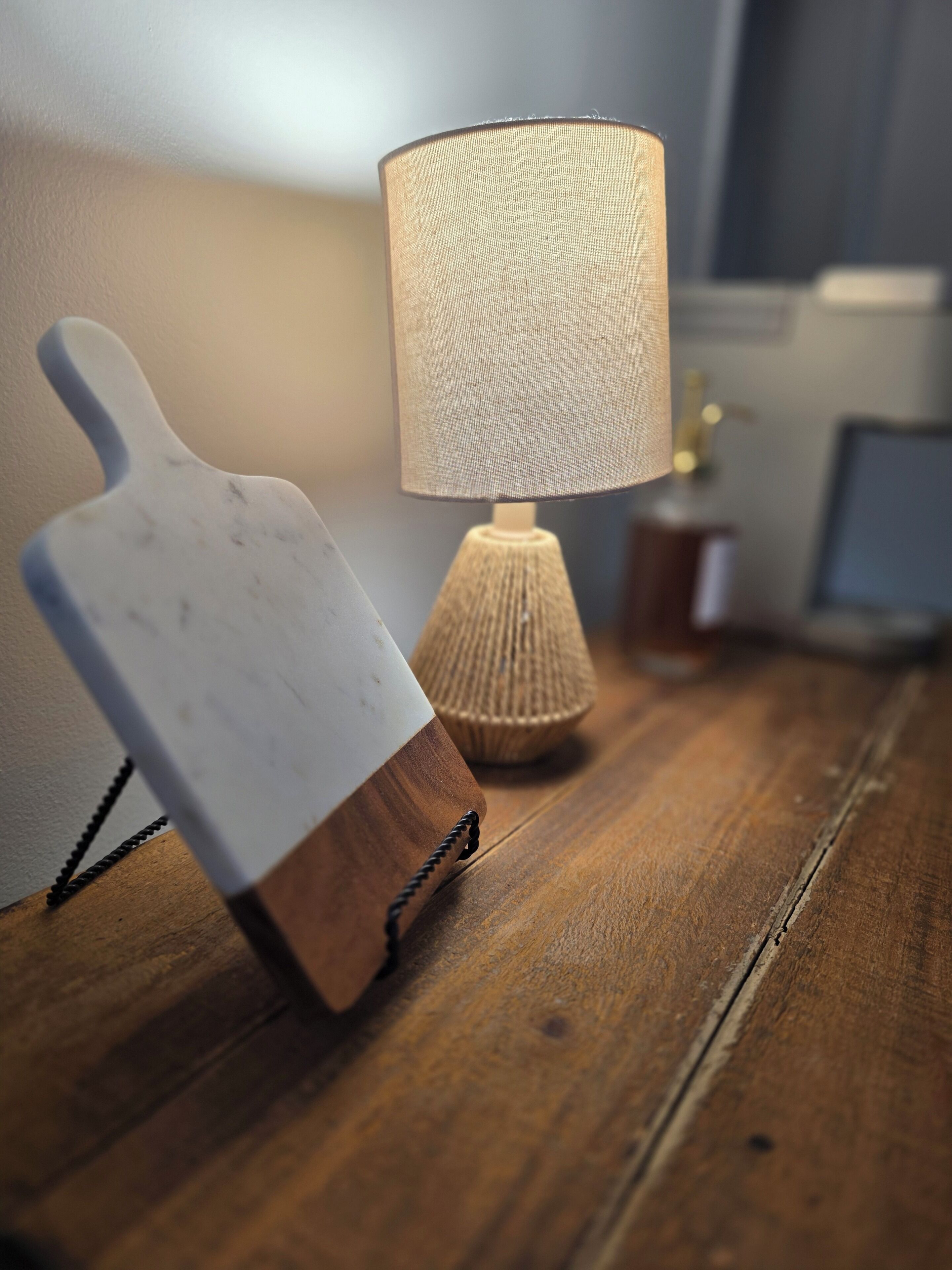 Een houten tafel met een wit snijplank en een lamp met een lichtkap met structuur.