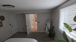 Un dormitorio con cama, una planta, un espejo y una puerta que da a otra habitación.