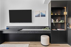 A modern living space with a flat-screen TV mounted on the wall, a marble countertop, a black cabinet with a shelf, and a round ottoman. - Luxury E11EVEN 22nd Floor Suite with City & Bay View (Miami)