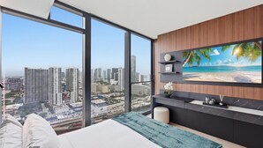 Un dormitorio con una ventana grande, una cama, un televisor y vista a la ciudad.