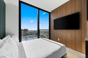 A modern bedroom with a large bed, a flat-screen TV mounted on the wall, and a city view through floor-to-ceiling windows. - 36th Floor E11EVEN Escape w/ Bay & City Views (Miami)