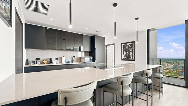 A modern kitchen with a central island, bar stools, and a large window offering a city view. - 44th Floor at E11EVEN with Panoramic City Views (Miami)