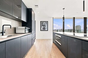 A modern kitchen with dark cabinetry, a large window, and a city view. - 44th Floor at E11EVEN with Panoramic City Views (Miami)