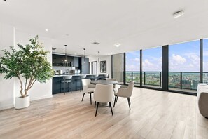 A modern kitchen with a dining area, a large potted plant, and a city view through large windows. - 44th Floor at E11EVEN with Panoramic City Views (Miami)