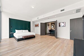 Ein modernes Schlafzimmer mit einem großen Bett, einer Bank, einem Kleiderschrank und einem durchgehenden Türrahmen einsehbarer Badezimmer.