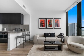 Ein modernes Wohnzimmer mit einer Couch, einem Couchtisch und Blick auf die Stadt durch große Fenster.
