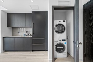 A modern kitchen with dark cabinetry, a sink, and a built-in washing machine. - 32nd Floor E11EVEN w/ Rooftop Pool & Skyline Views (Miami)