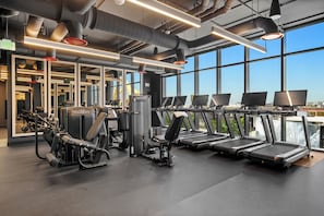 Ein Fitnessstudio mit Laufbändern, Krafttrainingsgeräten und großen Fenstern.