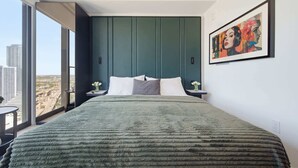 Quarto moderno com uma cama grande, vista para a cidade e uma obra de arte emoldurada na parede.
