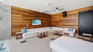 Uma sala de estar moderna com parede de madeira, uma TV de tela plana, sofás brancos, mesas de centro de madeira e um ventilador de teto.