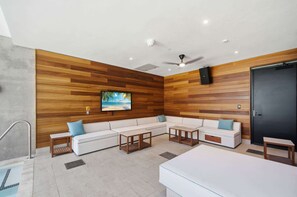 A modern living room with a wooden wall, a flat-screen TV, white sofas, wooden coffee tables, and a ceiling fan. - 15th Floor E11EVEN Retreat Near Miami Worldcenter (Miami)