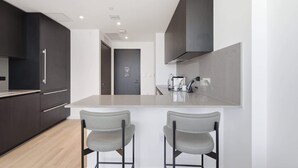 A modern kitchen with dark cabinetry, a central island with two bar stools, and a visible door in the background. - Stunning E11EVEN Residences Suite Rooftop Pool (Miami)