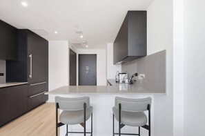 A modern kitchen with dark cabinetry, a central island with two bar stools, and a visible door in the background. - Stunning E11EVEN Residences Suite Rooftop Pool (Miami)