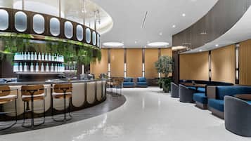 A modern bar area with a curved counter, bar stools, and a seating area with sofas and chairs.