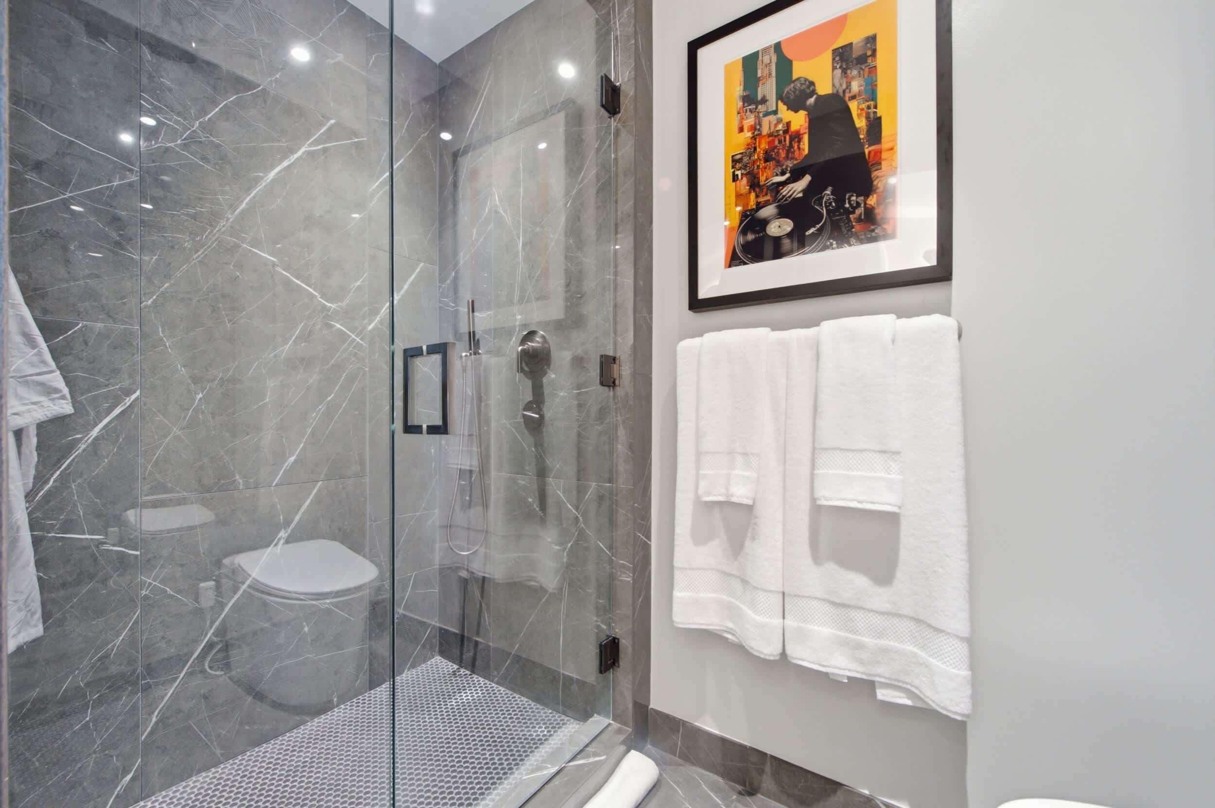 Une salle de bain moderne avec une douche à parois de verre, des toilettes et un tableau encadré au mur.