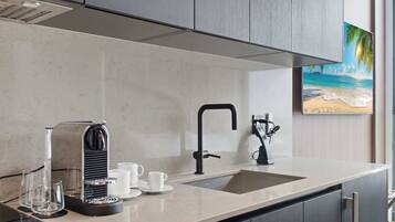 A modern kitchen with a coffee machine, sink, and a painting of a beach scene.