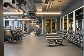 Ein Fitnessraum mit Trainingsgeräten, Kurzhanteln und einem großen Fenster.