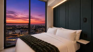 Une chambre avec une grande fenêtre, un lit et une vue sur la ville au crépuscule.
