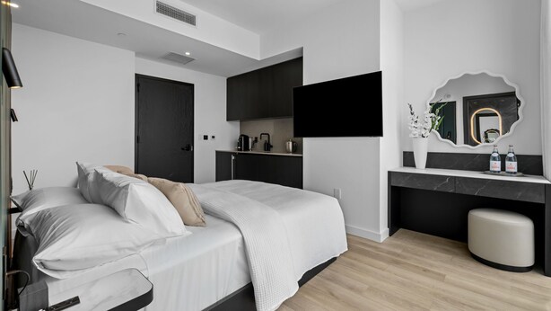 Un dormitorio moderno con cama, mesita de noche y un escritorio empotrado con espejo.