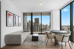 A modern living room with a gray sofa, a coffee table, and a dining area with chairs and a table. Large windows offer a city view. - 35th Floor E11EVEN Retreat with Skyline & Bay Views (Miami)