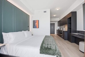 Ein modernes Schlafzimmer mit einem großen Bett, einer Bank und einer kleinen Küche im Hintergrund.