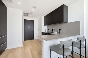 A modern kitchen with dark cabinets, a light countertop, and a bar area with two stools. - E11EVEN 25th Floor Residence w/ Skyline Views (Miami)