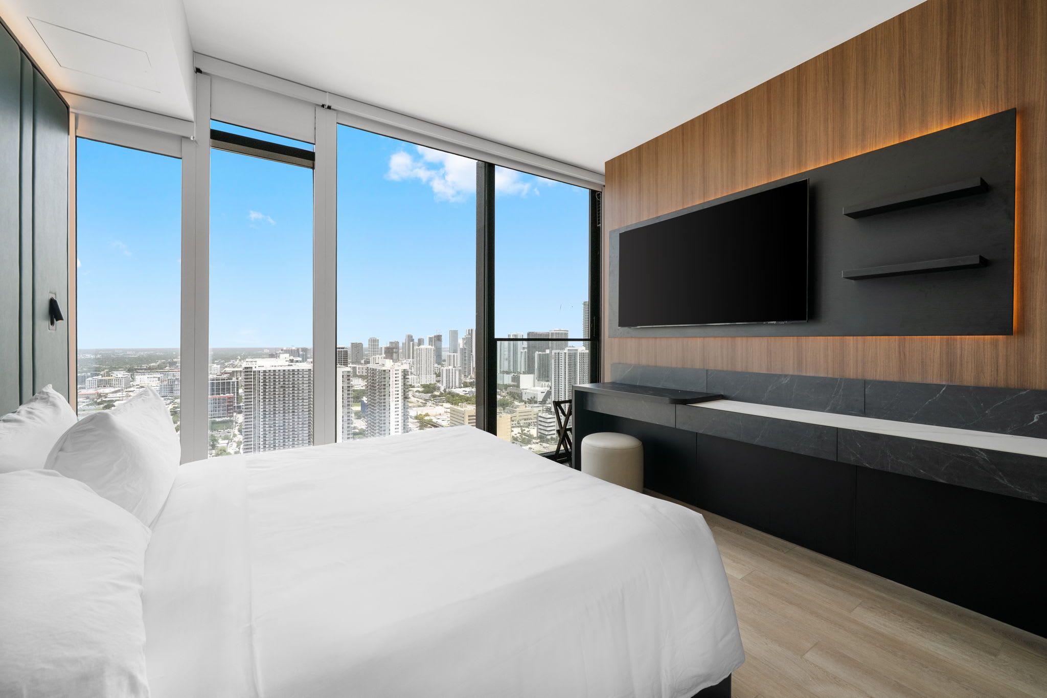 Une chambre d’hôtel moderne avec un grand lit, un téléviseur fixé au mur et une vue sur la ville.