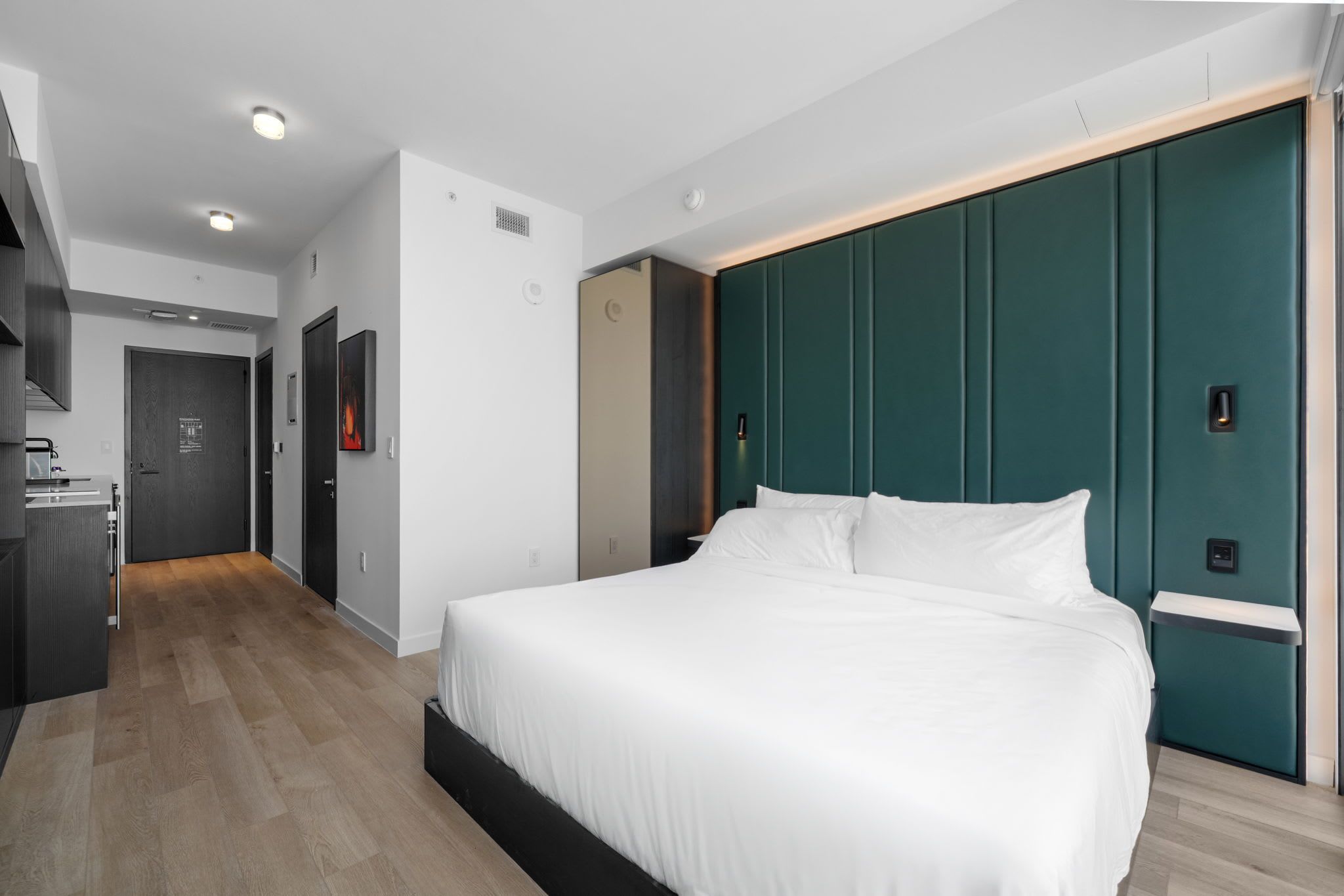 Una habitación de hotel moderna con una cama grande, un armario, un escritorio y una kitchenette.