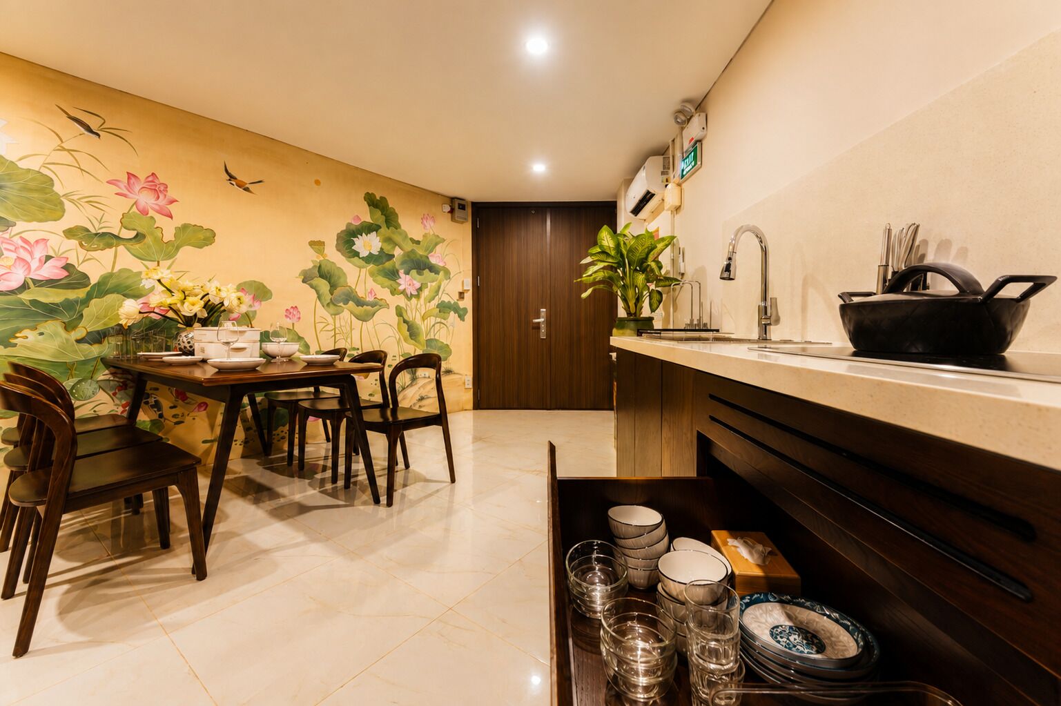 A dining area with a table set for four, a kitchen counter with a sink and utensils, and a wall with a floral mural.