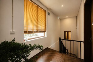 Una escalera con piso de madera, barandal negro y una ventana con persianas.