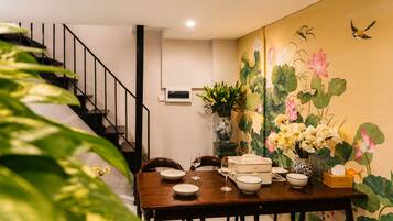 Un comedor con una mesa de madera dispuesta para dos personas, un jarrón con flores y una escalera al fondo.