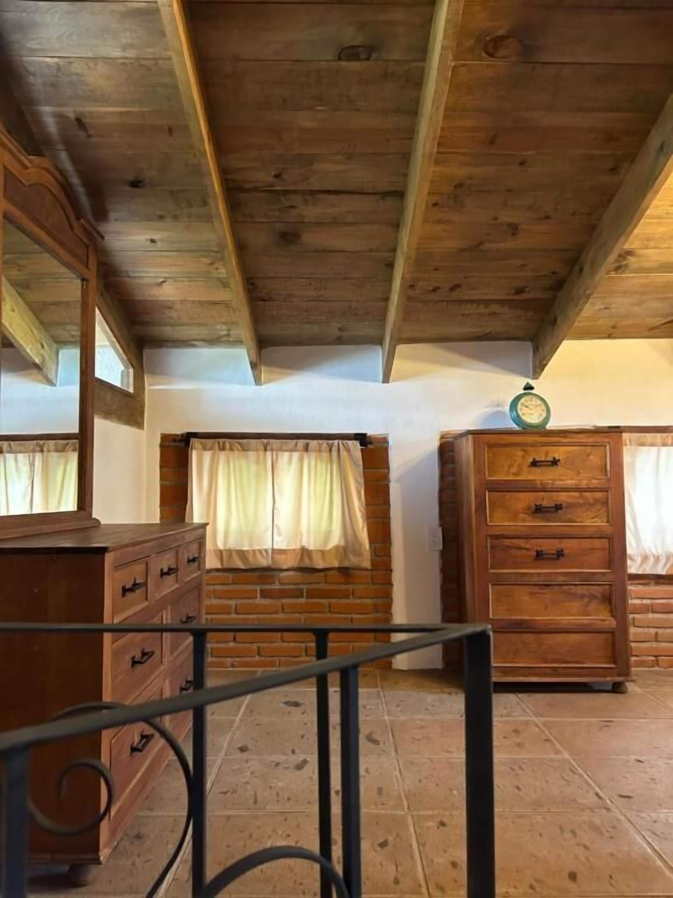 Een kamer met houten balken in het plafond, een bakstenen muur en twee houten kasten met lades.