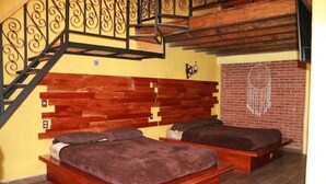 A bedroom with two wooden beds, a brick wall, and a staircase with ornate railings.