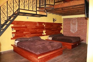 A bedroom with two wooden beds, a brick wall, and a staircase with ornate railings.