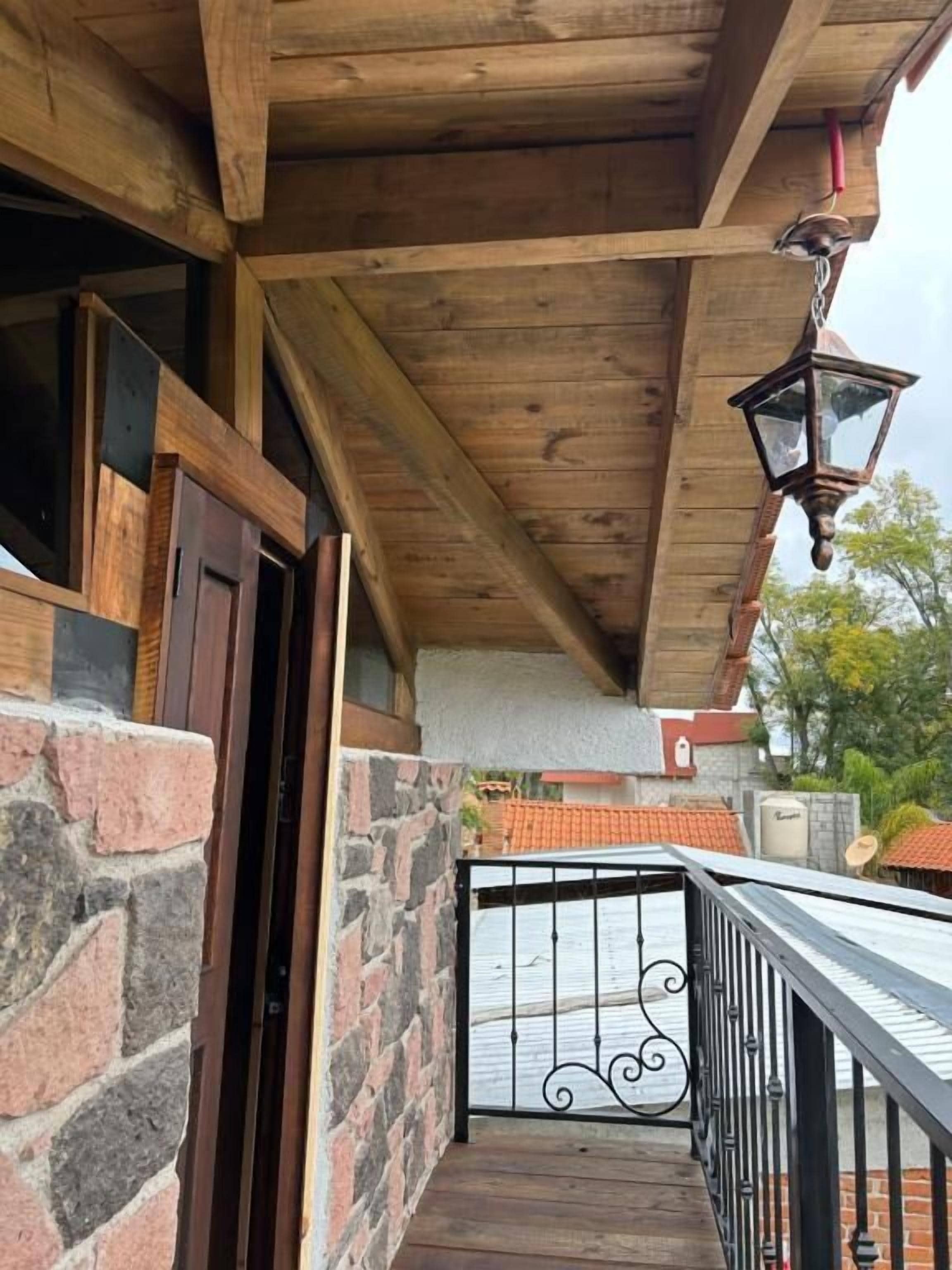 Un balcón de madera con barandilla de metal, una pared de ladrillo y techo de madera.