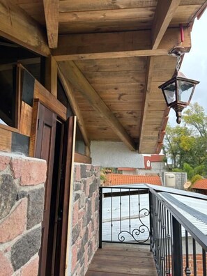 A wooden balcony with a metal railing, a brick wall, and a wooden ceiling. - Cabañas del Bosque (San Miguel Regla)