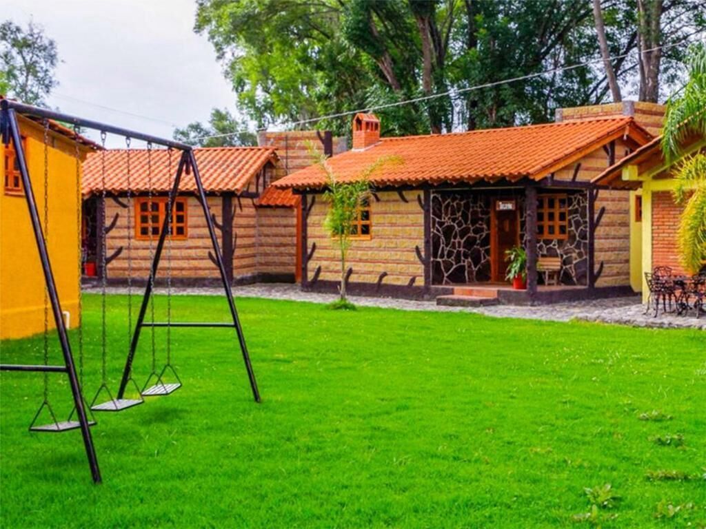 Una casa de madera rústica con techo de tejas rojas, un columpio y un césped bien cuidado.