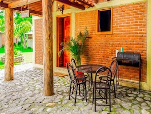 An outdoor patio with a brick wall, a round table with chairs, and a grill.