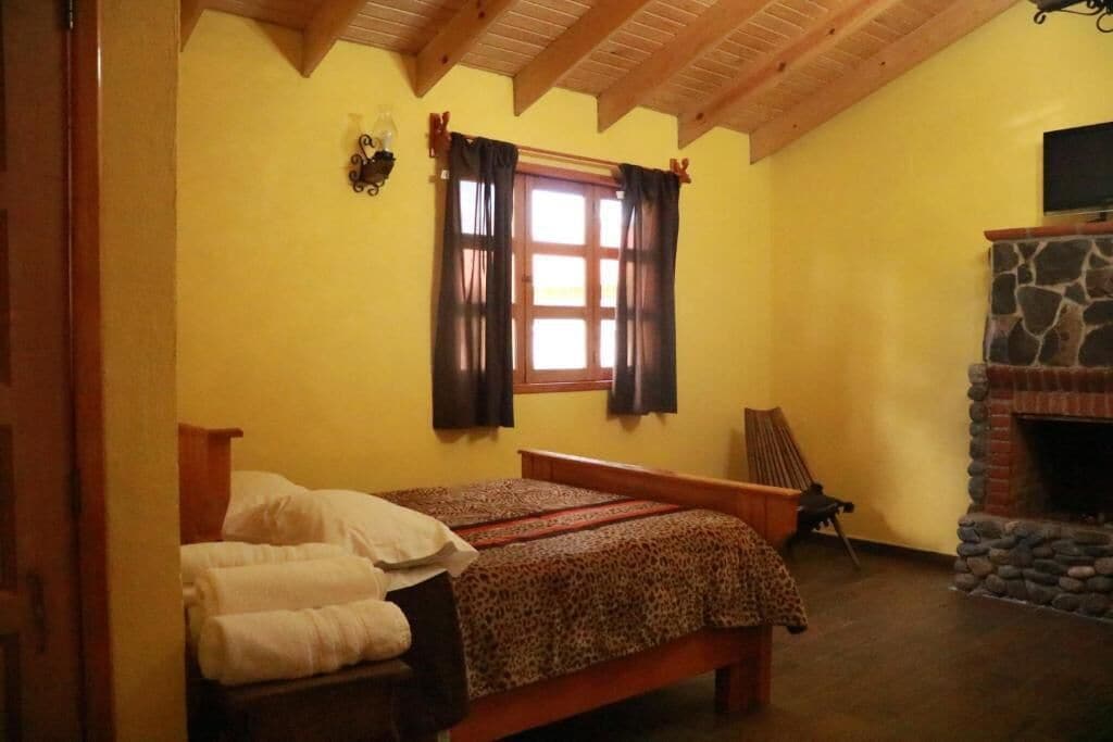 A bedroom with a bed, a stone fireplace, and a window with curtains.