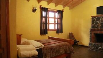 A bedroom with a bed, a stone fireplace, and a window with curtains.