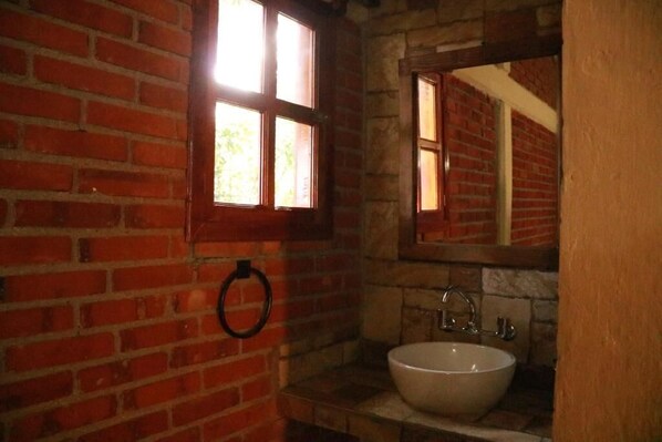 Une salle de bain avec un lavabo blanc, un miroir et une fenêtre donnant sur un mur de briques.