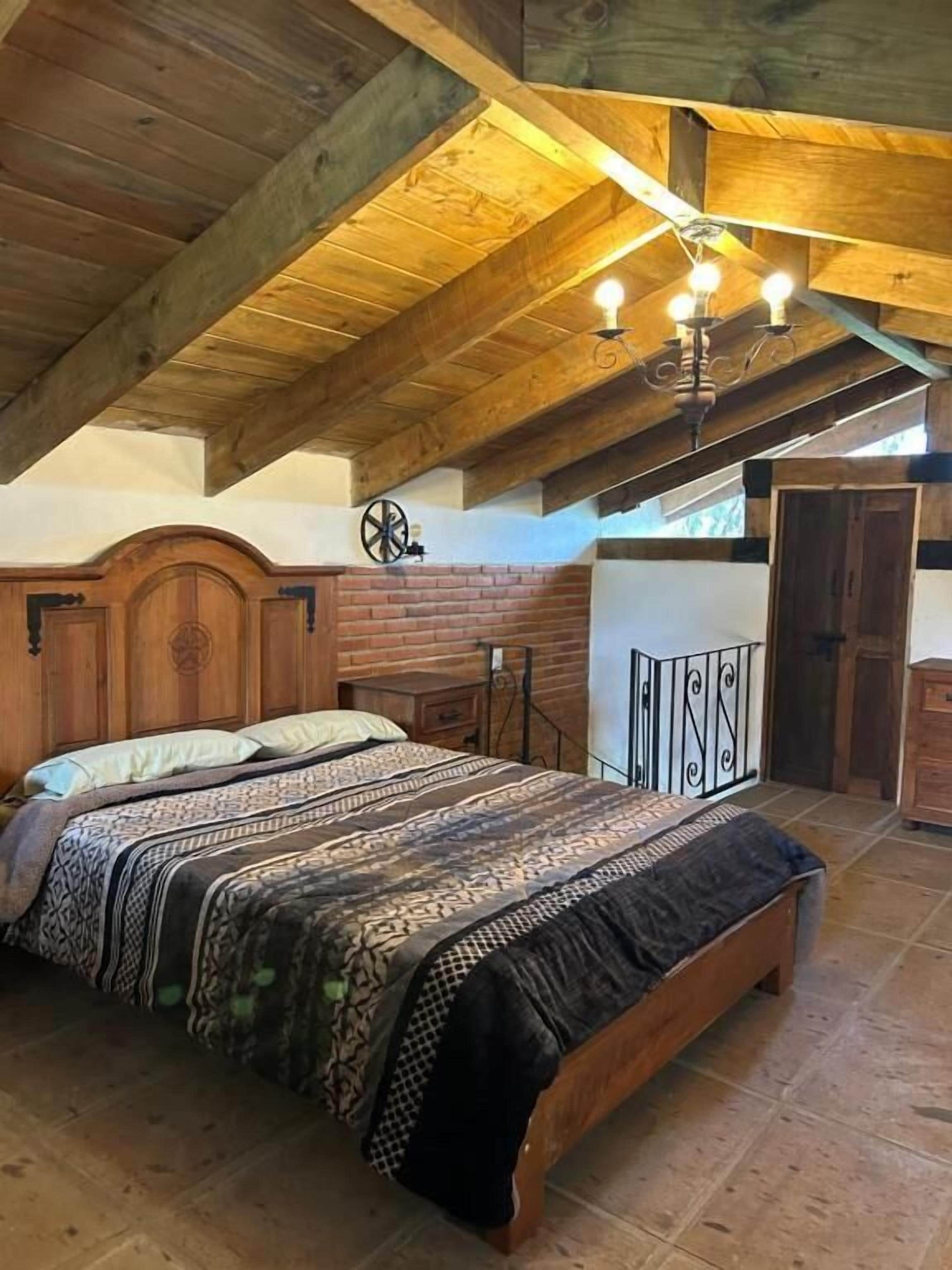 Un dormitorio con techo de madera, una cama con ropa de cama estampada, una mesita de noche y un reloj de pared.