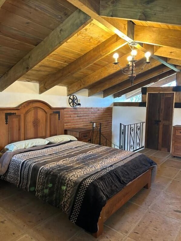 A bedroom with a wooden ceiling, a bed with patterned bedding, a nightstand, and a wall clock. - Cabañas del Bosque (San Miguel Regla)