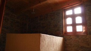 A room with a stone wall, a wooden ceiling, and a window with six panes.
